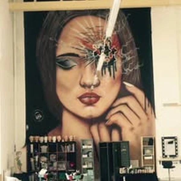 Large-scale airbrushed mural of a woman’s face with makeup and a shattered-glass effect, covering an entire interior wall of a salo