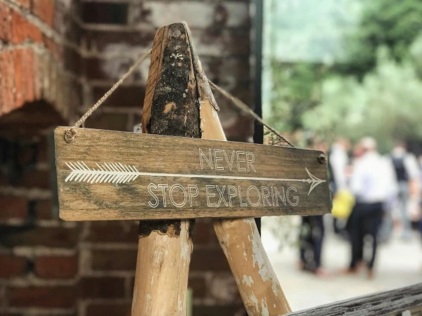 Fából készült tábla nyíllal: "Never stop exploring" – felfedezésre hívás