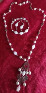 White gemstone necklace, bracelet, and earrings set with rose-shaped metal charms on a red background
