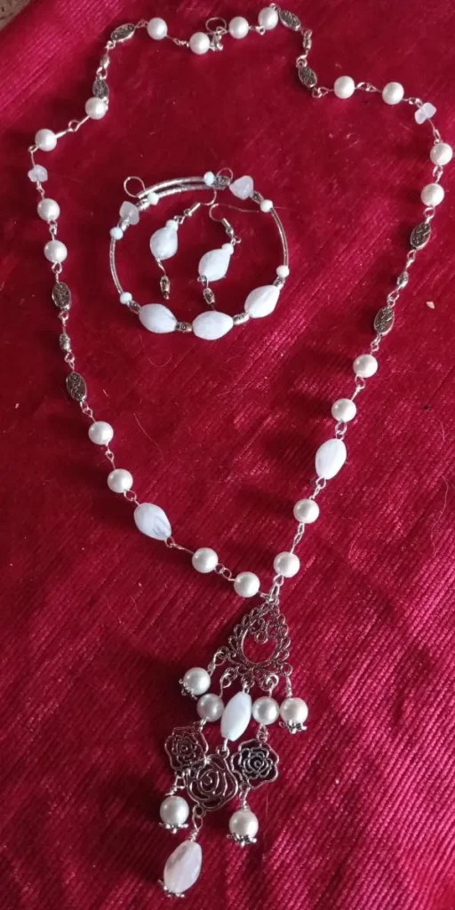 White gemstone necklace, bracelet, and earrings set with rose-shaped metal charms on a red background