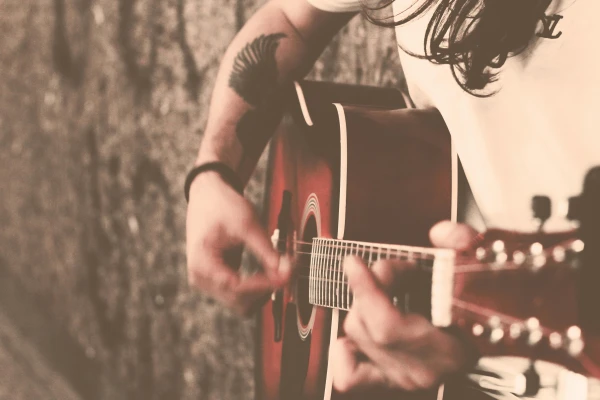 Close-up of a long-haired guitarist playing an acoustic guitar passionately, with a tattoo visible on the arm