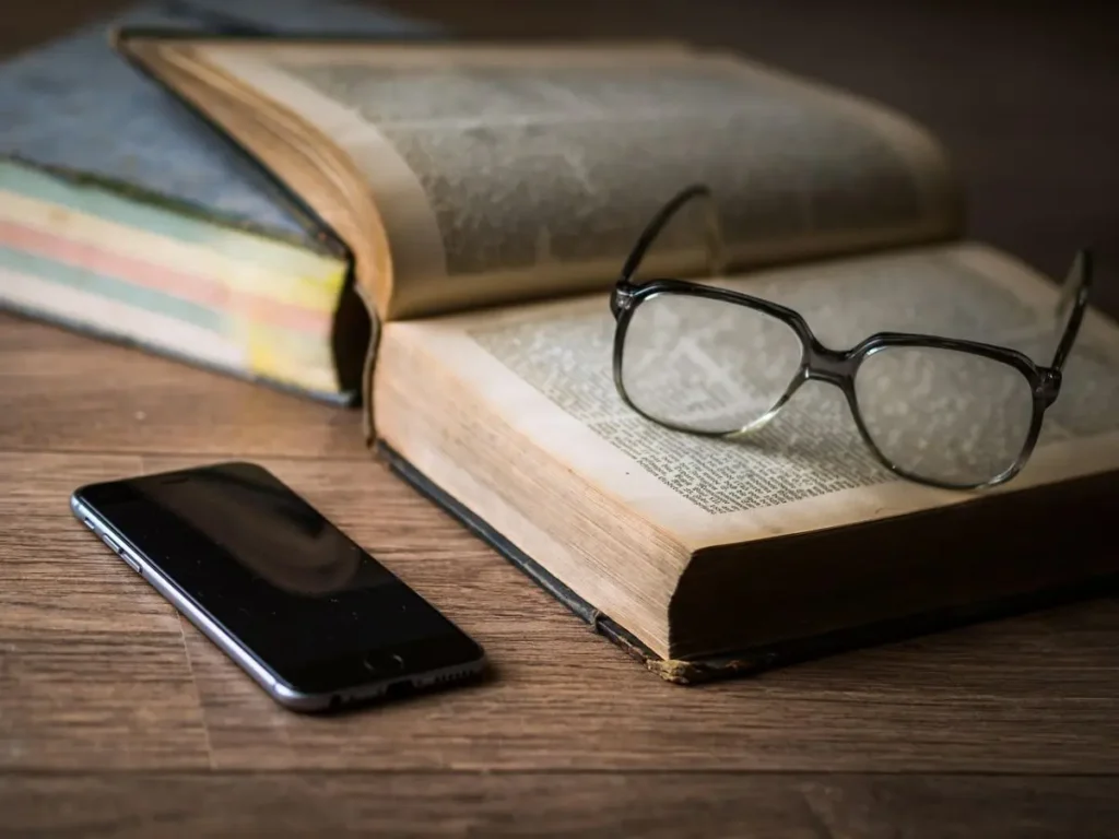 Nyitott könyv szemüveggel és telefonnal – a Bookworm, Podcast és Bridge Audio szobák szimbóluma a Vig-Village-ben”