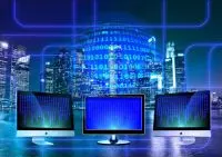 Three computer monitors in front of a glowing city skyline with binary code overlaid, representing a global digital AI network.