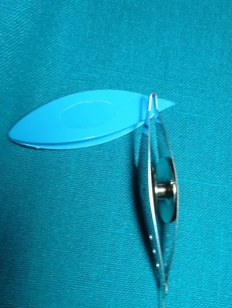 Tatting technikához használt kézi szerszám: egy kék műanyag és egy fémből készült csónak alakú fonalvezető