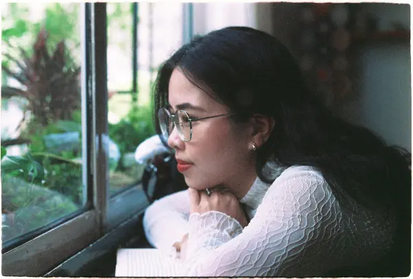Young woman gazing out the window, resting her chin on her hands.