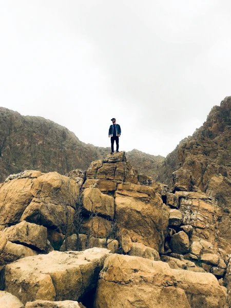A person standing on top of rocky cliffs – symbol of perseverance and reaching a goal