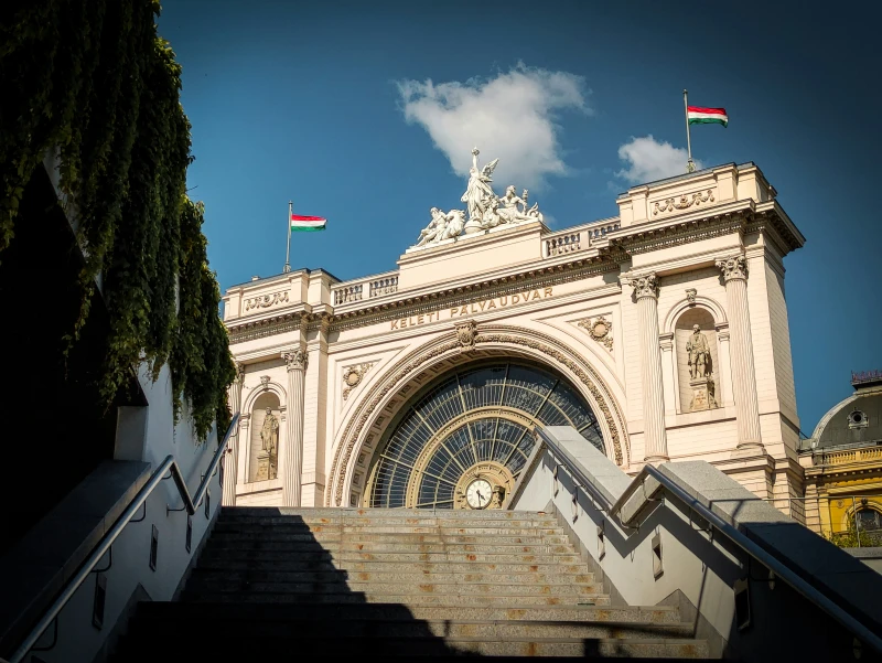 Lépcsőn felfelé haladva tünik fel a pályaudvar hatalmas homlokzatának egy része. Félkör alakú üveg mellett kétoldalt bástyaszerű épületrész. Tetején szoborcsoport.