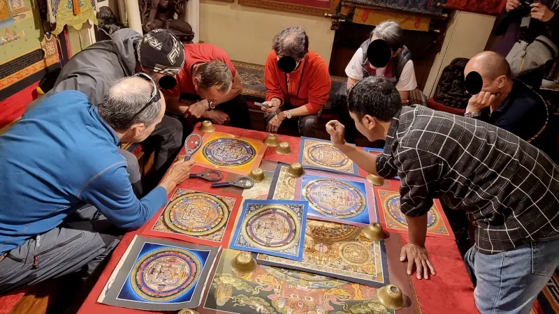 Six people are sitting around a low table. The seventh leans over the table and tries to aim at something. There are square boards with circle patterns on the table. Some people are talking to each other, others are watching them.