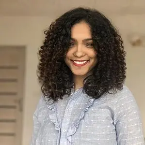 A smiling young woman with dark, curly hair and Creole skin. She is wearing a light blue blouse.