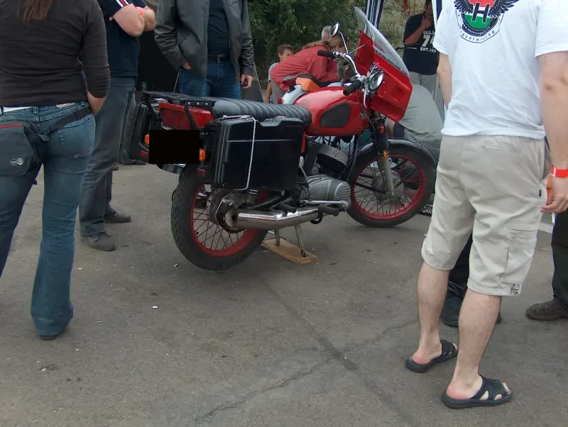 Emberek vesznek körül egy piros-fekete motort. Fejük nem látszik a képen
