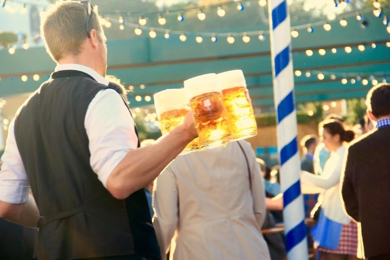 Egy lampionokkal díszített pavilonban sok ember, előtérben egy pincér. Egyik kezében legalább négy darab literes söröskorsó van.