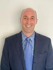 A smiling young man wearing a blue suit. It is not apparent how funny he usually is.