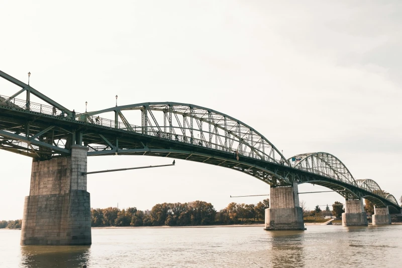 The bridge is visible, photographed slightly from below, from one of the banks. There are four arched iron structures and four bridge piers in the picture.