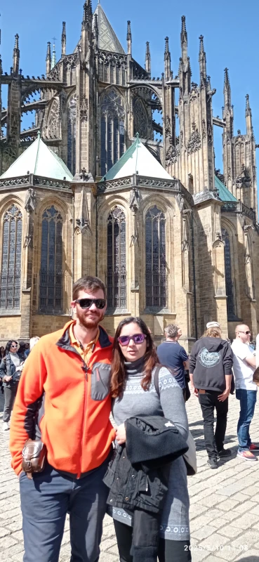 In the foreground, a young couple, the young man wearing an orange top. In the background, the dark walls of the cathedral, with thousands of towers, three angular naves, topped with green tent roofs.