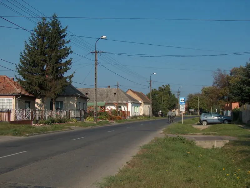 Aszfaltos utca Sárospatakon, két oldalt családi házakkal, előtérben buszmegálló tábla.