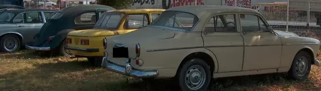 Sárga és zöld veterán autók parkolva egymás mellett, háttérben kerítéssel