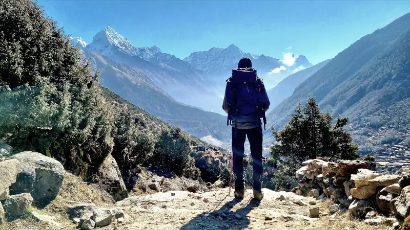 A traveler standing on top of a mountain looks toward even higher peaks in the distance.