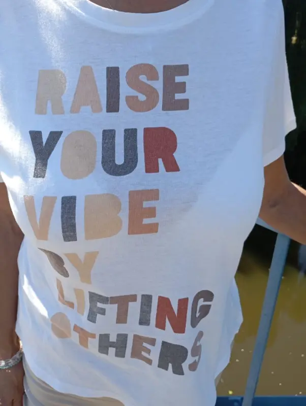 Egy póló ezzel a felírattal: "Raise your vibe by lifting others". Vidíts fel másokat, hogy te is felvidulj