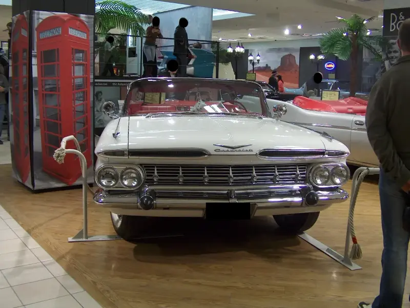 Egy Chevrolet Impala Convertible-1959 elölről fotózva. Körülötte korabeli díszletek például egy telefonfülke