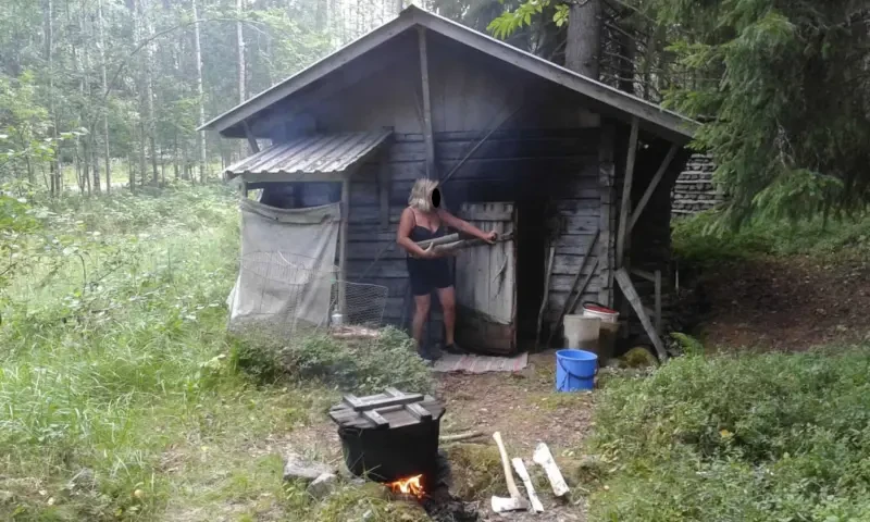Egy öreg, füstös szauna egy hölggyel, aki fát visz be . Az udvar előterében egy üstben épp főznek valamit.