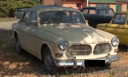 Old beige Volvo car parked, with other vintage cars in the background