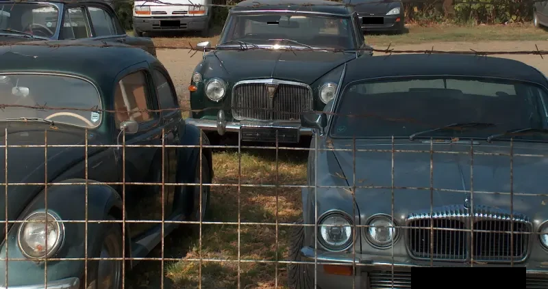 Old Jaguar and Volkswagen cars parked behind a fence in Sárospatak